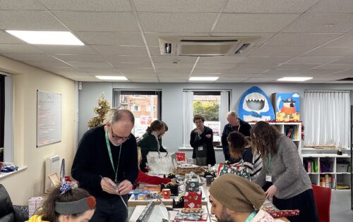 a group of people chat and wrap Christmas presents on a large table