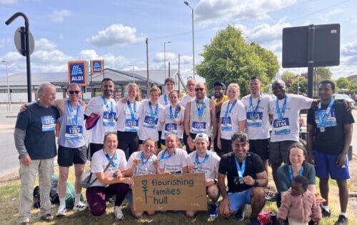 A group of runners dressed in white smiling with their medals, holding up a sign